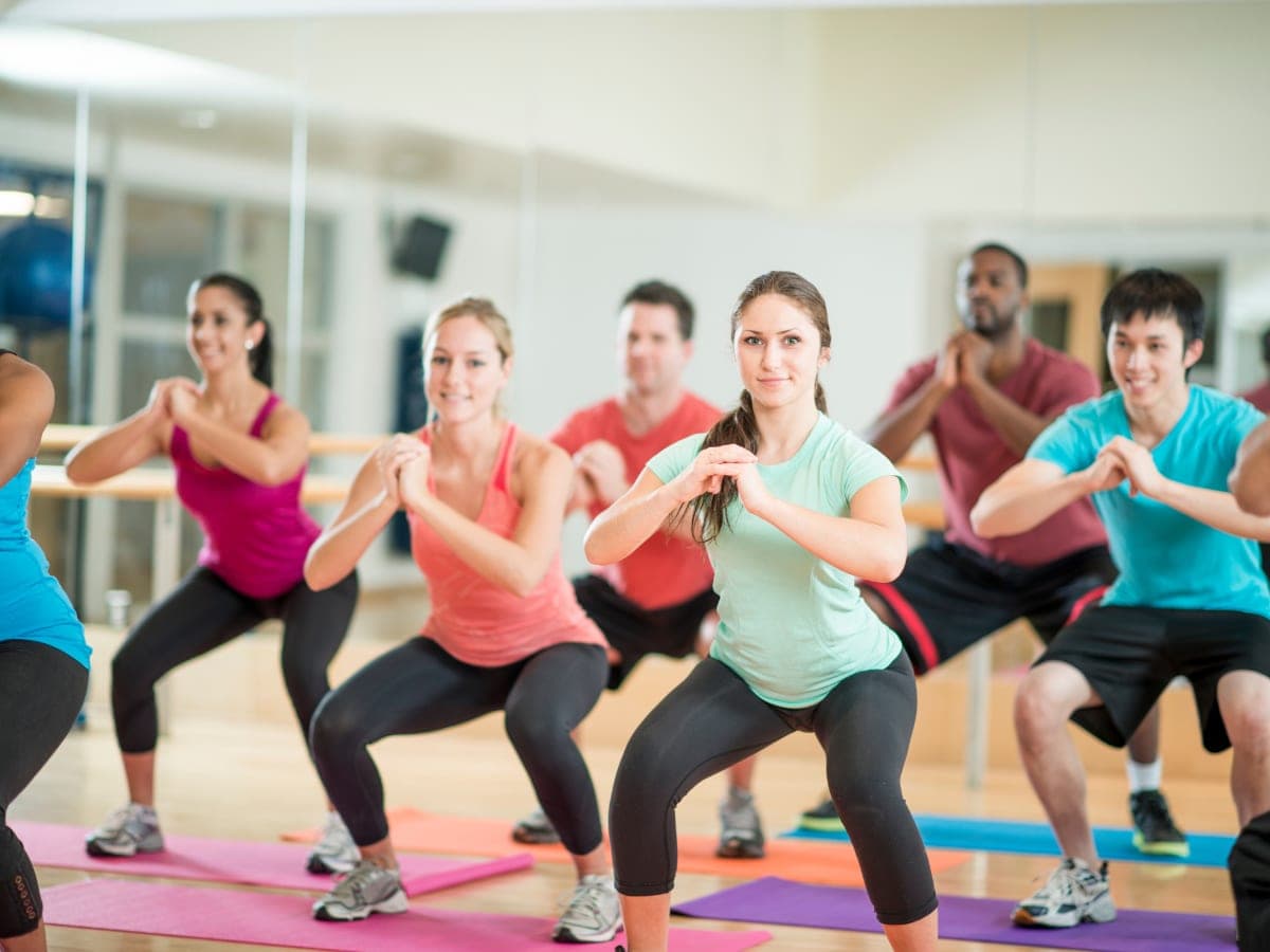 A host leading an energetic group fitness class in a bright studio